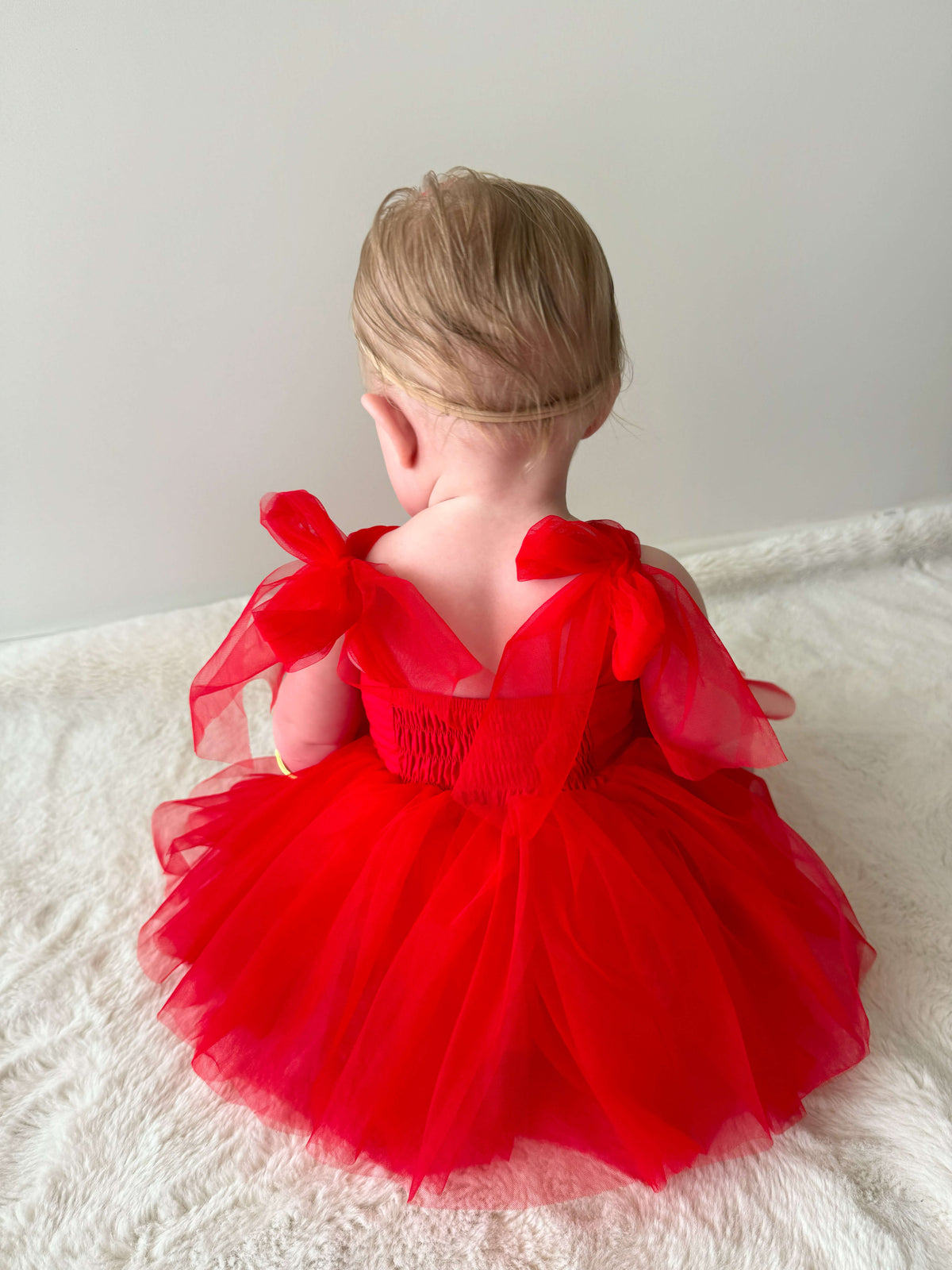 Back details of our Harper romper in ruby red being worn by a baby girl.