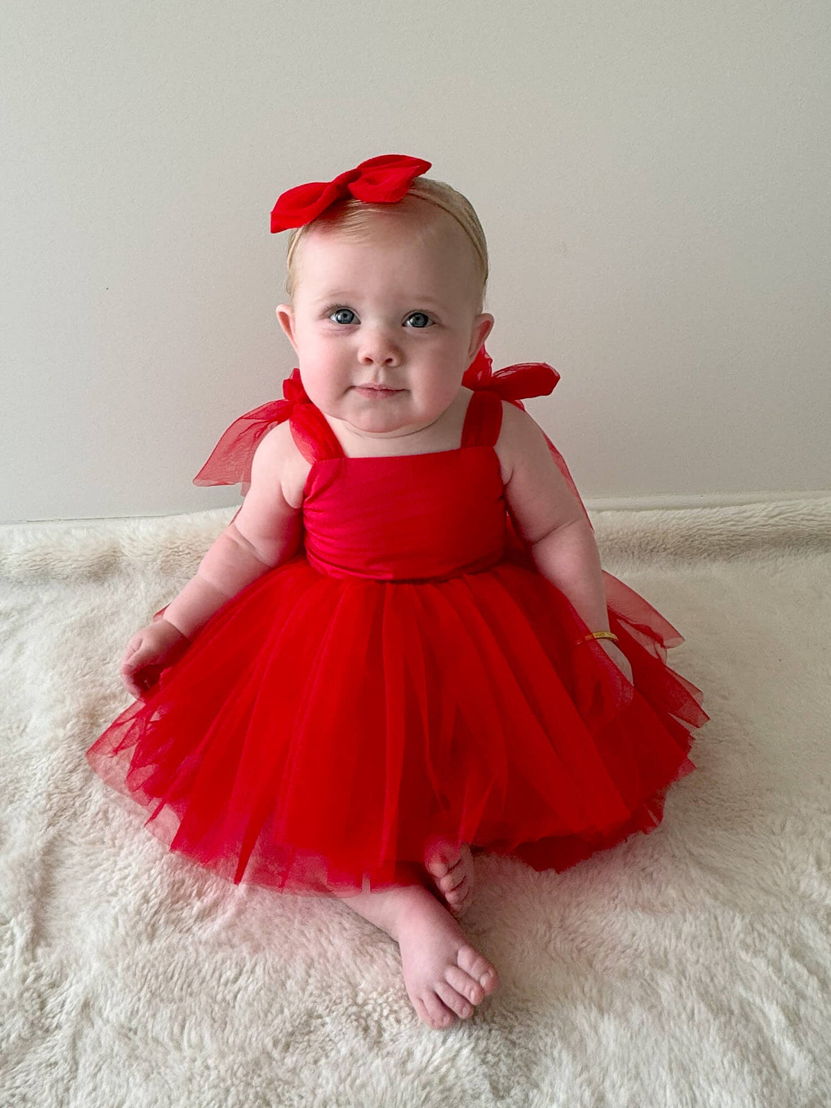 A baby sits wearing our ruby red Harper Christmas romper and matching tulle headband.