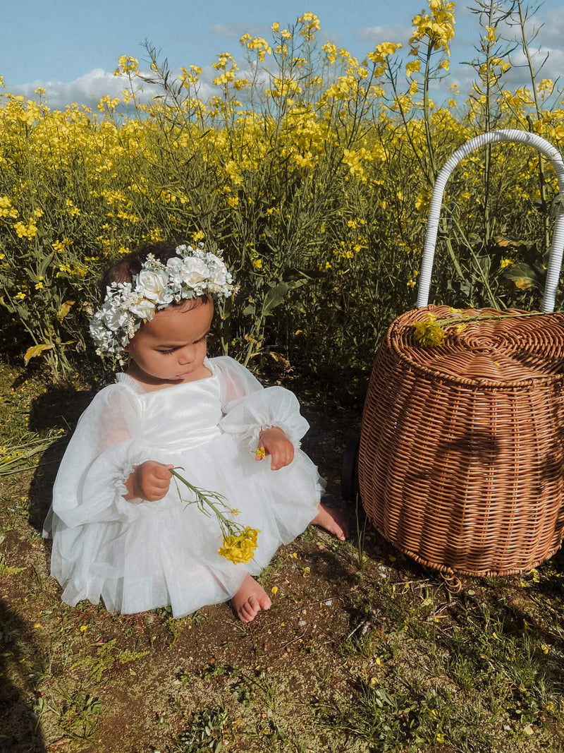 Eva baby flower girl romper in ivory is worn by a young girl, she also wears an ivory flower crown.