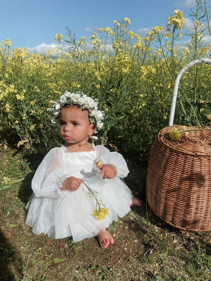 Eva baby flower girl dress is worn by a baby girl. She sits in a flower field holding a flower.