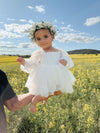 A toddler is held by her father wearing our Eva baby flower girl romper in ivory. She also wears an ivory flower crown. 