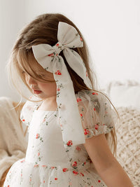 A young girl wears our red floral embroidered organza hair bow.