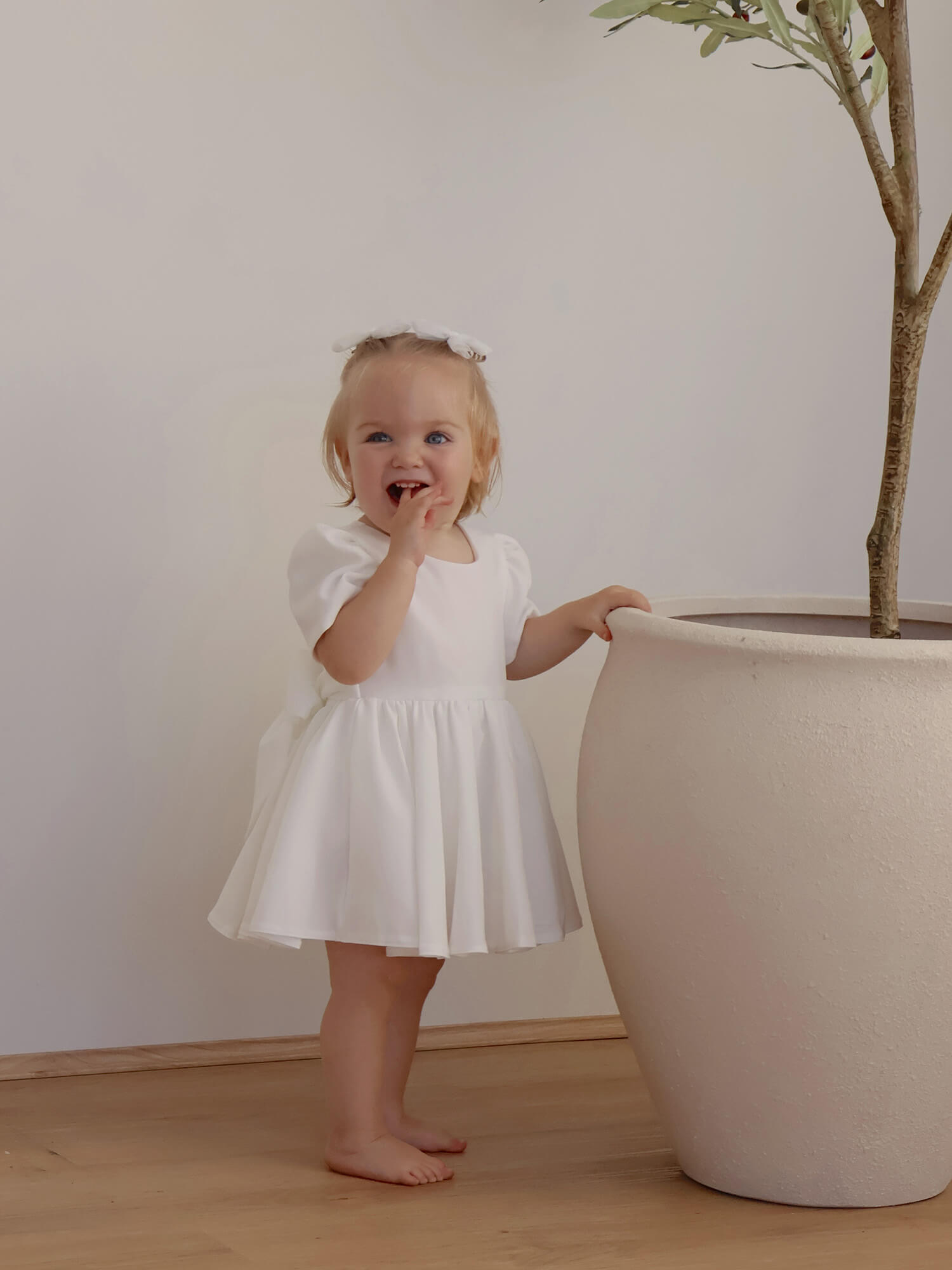 A toddler wears a white crepe flower girl dress.