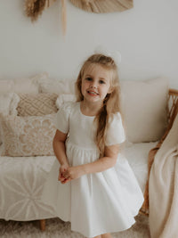 A young girl smiles, wearing our satin ivory flower girl dress, the Charlotte dress.