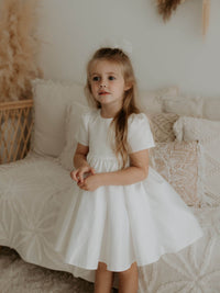A young girl stands wearing our Charlotte ivory satin flower girl dress.