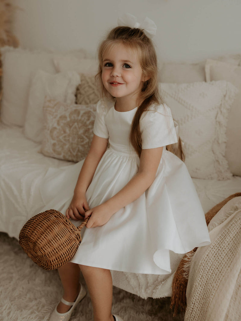 A young girl smiles, holding a basket, wearing our Charlotte ivory flower girl dress.