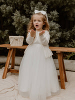 Chloe flower girl cardigan is worn by a toddler who is standing. She wears a satin and tulle flower girl dress and our Adeline satin bow in her hair.