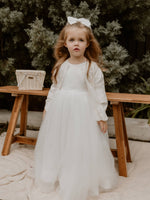 A toddler wears our Chloe flower girl cardigan along with a winter flower girl dress and a satin bow in her hair.