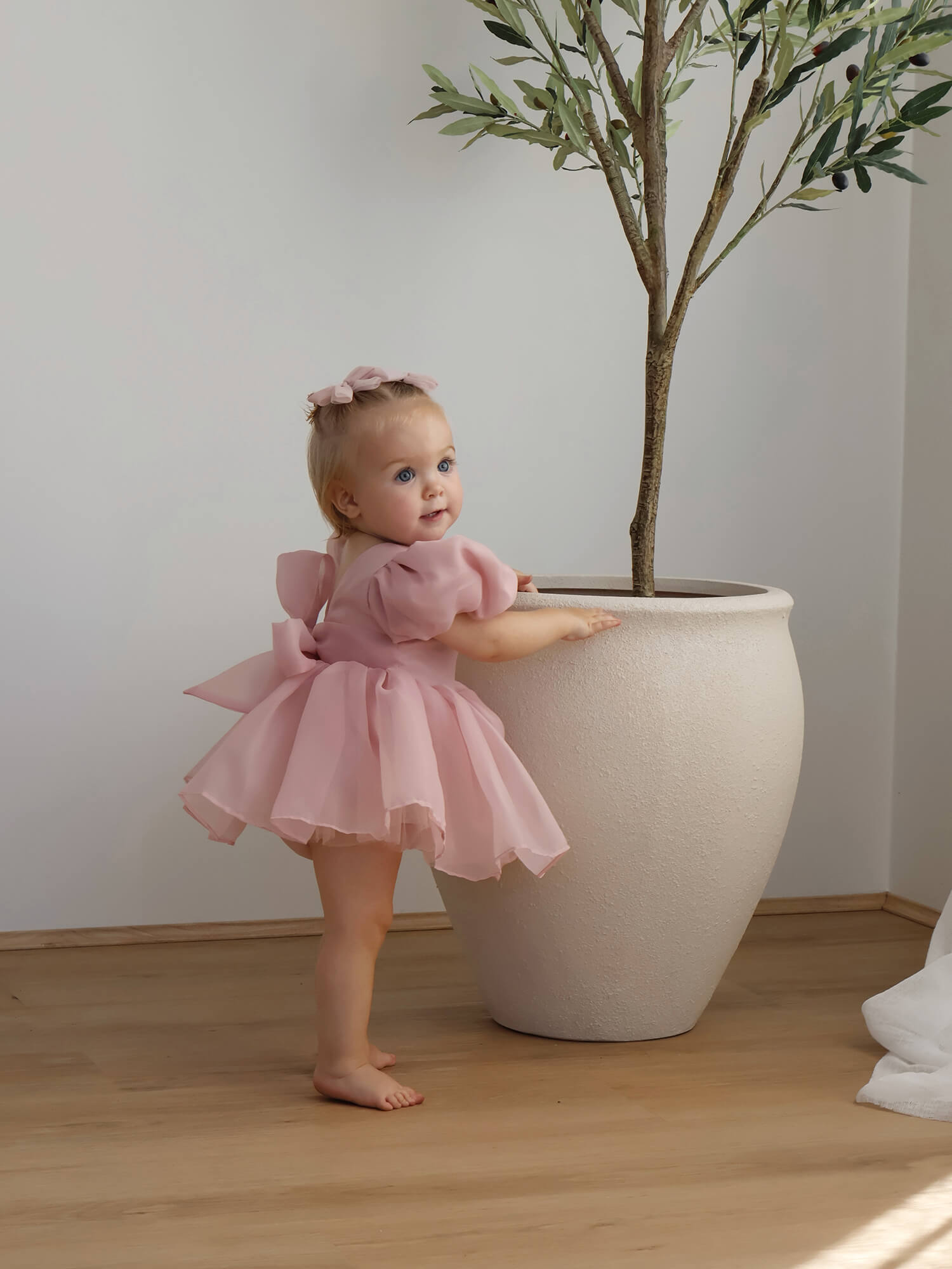Cleo blush baby flower girl romper is worn by a toddler, with matching tulle bows in her hair.