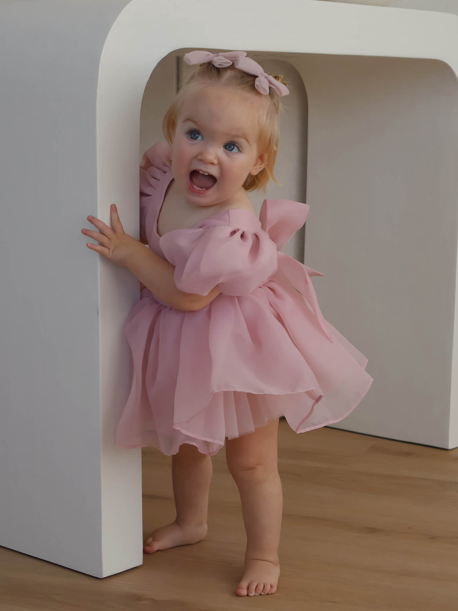 A little girl wears our Cleo blush puff sleeve baby flower girl romper.