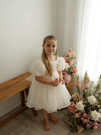 A little girl in our Cleo flower girl dress with cream organza and puff sleeves.