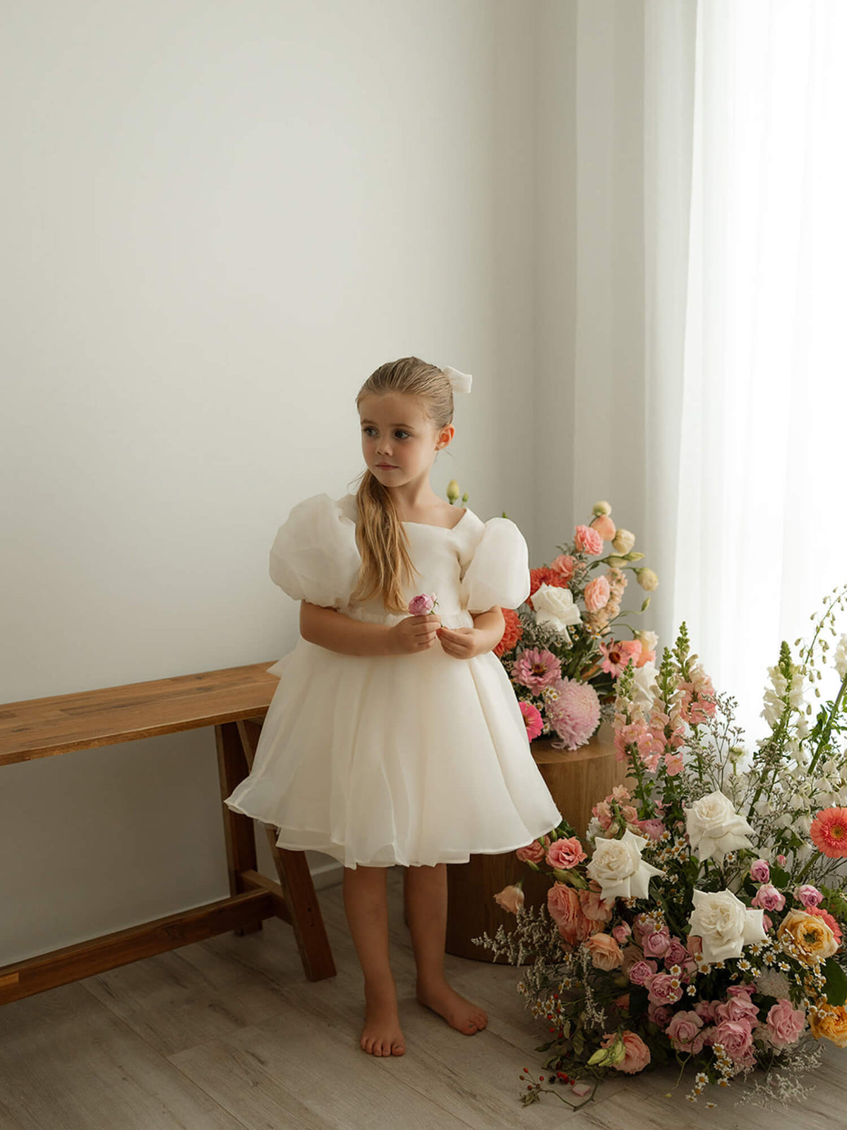 A young girl wears our elegant cream Cleo flower girl dress with puff sleeves, perfect for weddings.