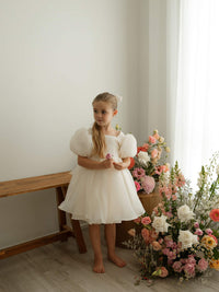 A young girl wears our elegant cream Cleo flower girl dress with puff sleeves, perfect for weddings.