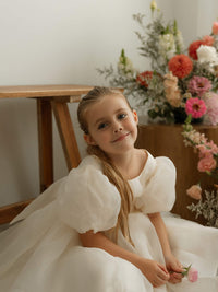 The Cleo dress in cream organza, a whimsical and classic flower girl outfit for weddings, is worn by a young girl.