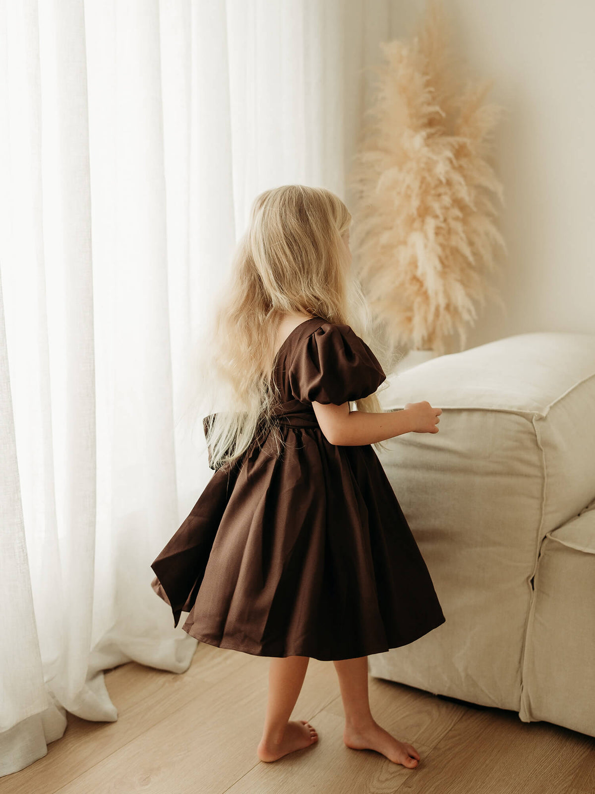 Cleo chocolate brown crepe flower girl dress is worn by a young girl who is twirling.