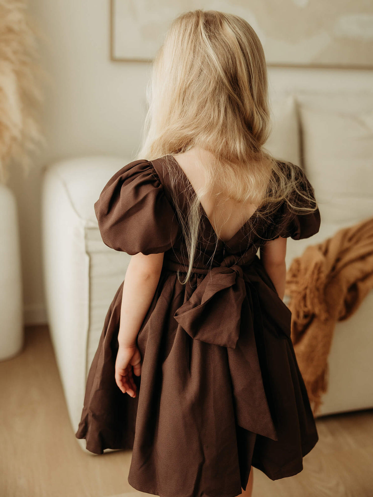 Cleo chocolate brown flower girl dress shown from the back, showing the large bow at the back and the puff sleeves.