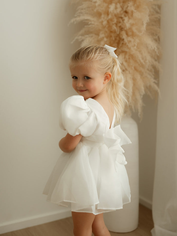 A young girl wears our Cleo ivory organza puff sleeve baby flower girl romper.