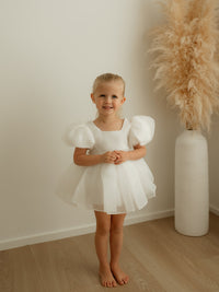 A little girl smiles wearing our Cleo ivory toddler flower girl dress, with puff sleeves.