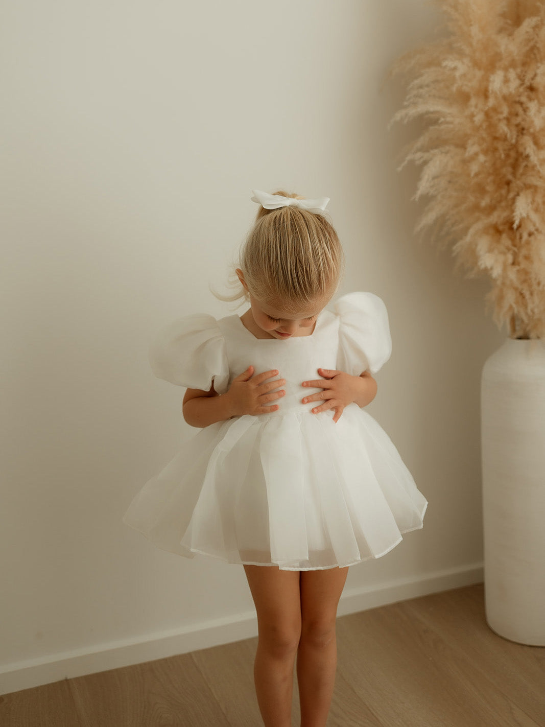 A little girl wears our Cleo puff sleeve baby romper and matching organza hair bow.