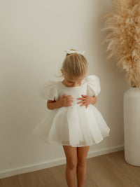 A little girl wears our Cleo puff sleeve baby romper and matching organza hair bow.