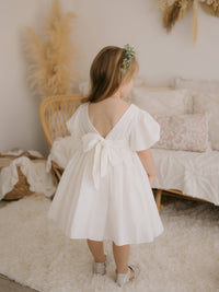 Cleo linen puff sleeve flower girl dress shown from the back. Showing the V back with linen bow.