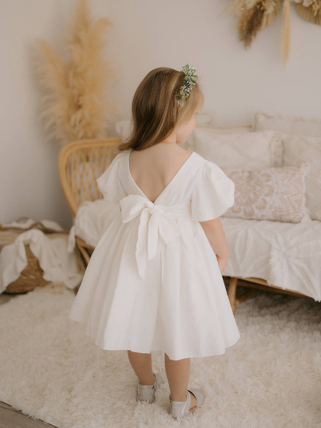 Cleo linen puff sleeve flower girl dress is worn by a young girl. she holds a flower girl basket and wears a floral wreath in her hair.