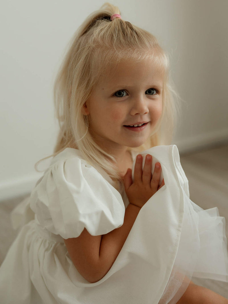 A little girl sits wearing our Cleo linen flower girl romper for babies and toddlers.