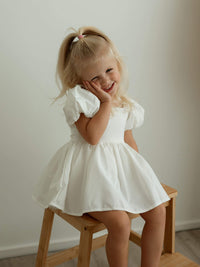 Cleo linen baby flower girl romper is worn by a smiling toddler.