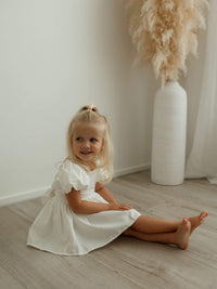 Cleo linen baby flower girl romper with puff sleeves is worn by a toddler.