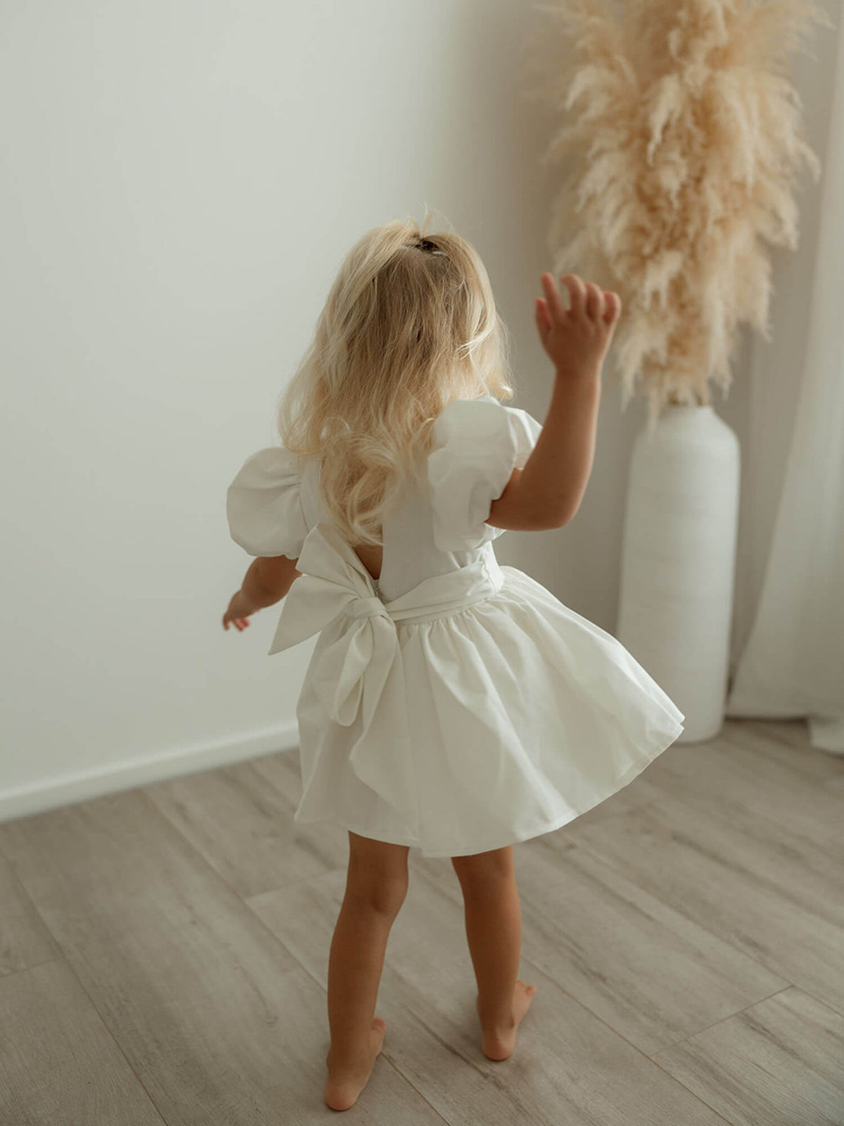 A little girl twirls wearing our Cleo baby flower girl romper with puff sleeves in linen.