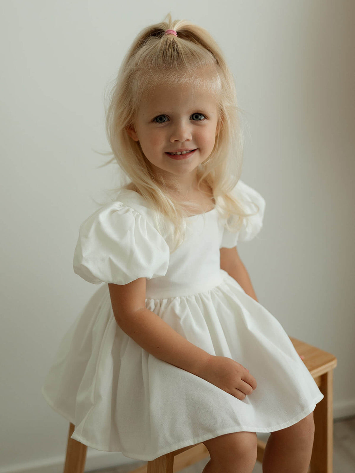 A toddler sits wearing our Cleo linen puff sleeve baby flower girl dress.