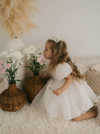 Cleo flower girl dress and medium tulle bow in ivory are worn by a young girl.