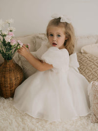 Cleo organza puff sleeve flower girl dress is worn by a young girl who is playing with flowers.
