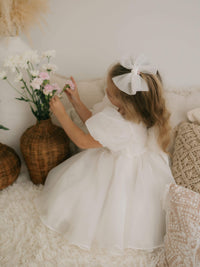 Ivory tulle bow hair clip and Cleo puff sleeve flower girl dress are worn by a young girl.