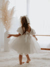 Cleo organza flower girl dress is worn by a young girl who is twirling in the dress, showing the dress from the back with the organza bow.