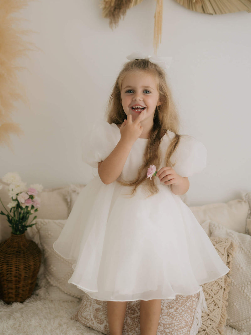 A young girl holds a flower, wearing our Cleo ivory organza flower girl dress and tulle hair bow.