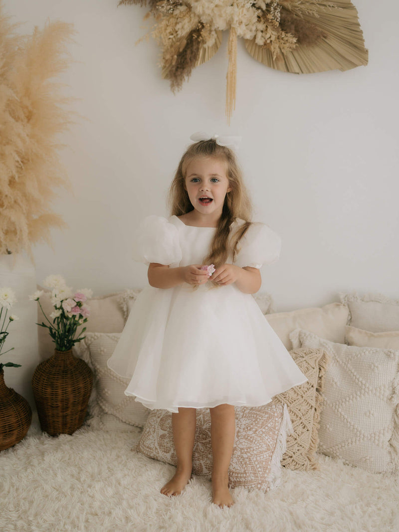 Cleo puff sleeve flower girl dress is worn by a young girl, she also wears an ivory tulle bow hair clip.