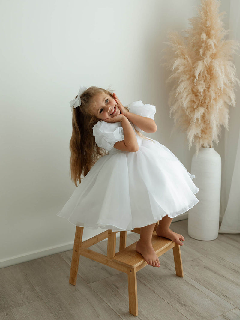 A little girl smiles wearing our Cleo flower girl dress in pure white.