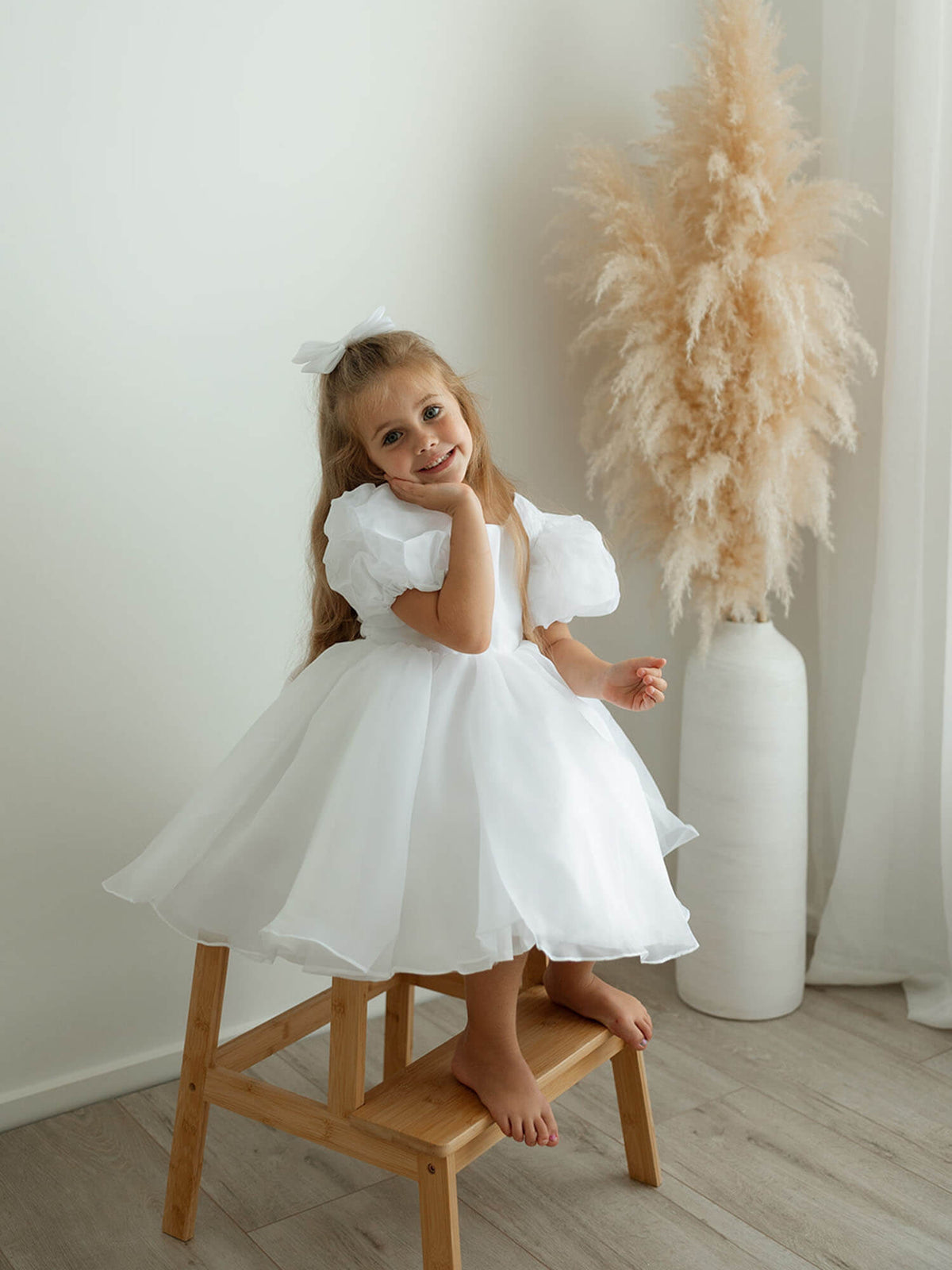 Pure white flower girl dress, our Cleo dress, is worn by a young girl sitting on a step.