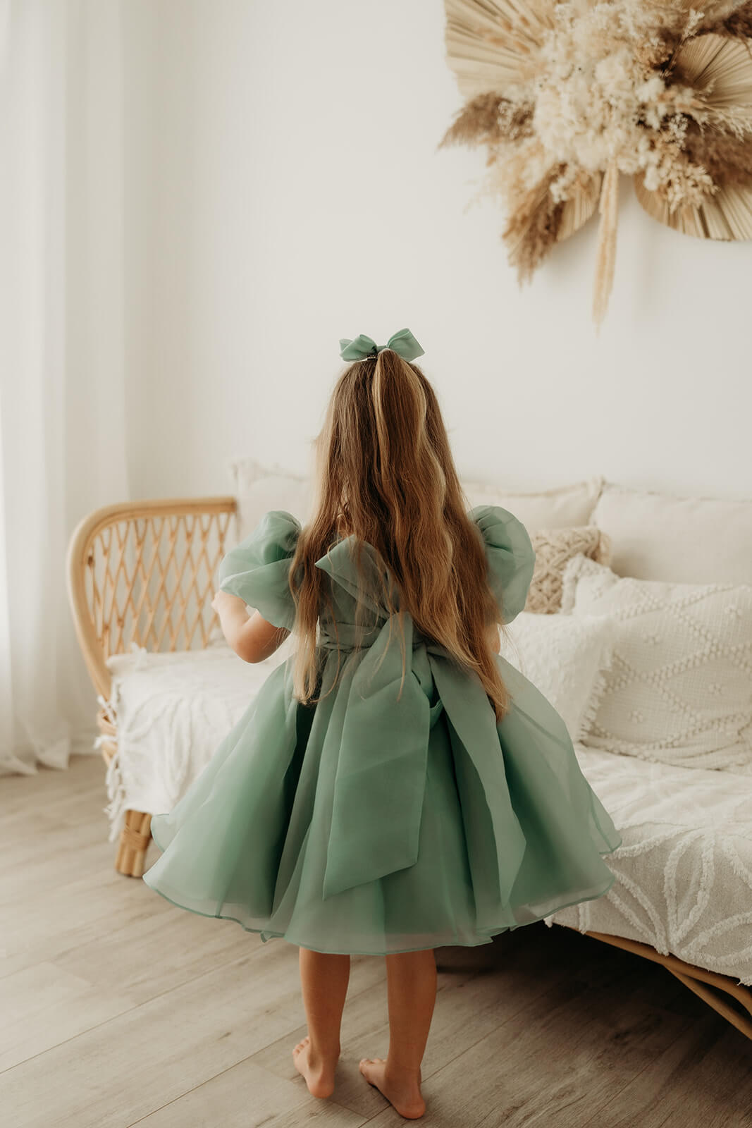 The back of our Cleo flower girl dress in jade, worn by a young girl. Showing the oversized bow at the back and the puff sleeves.