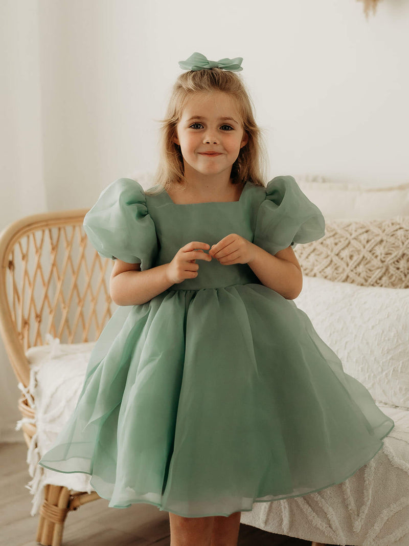 Cleo jade green flower girl dress is worn by a young girl. She also wears a matching organza hair bow.