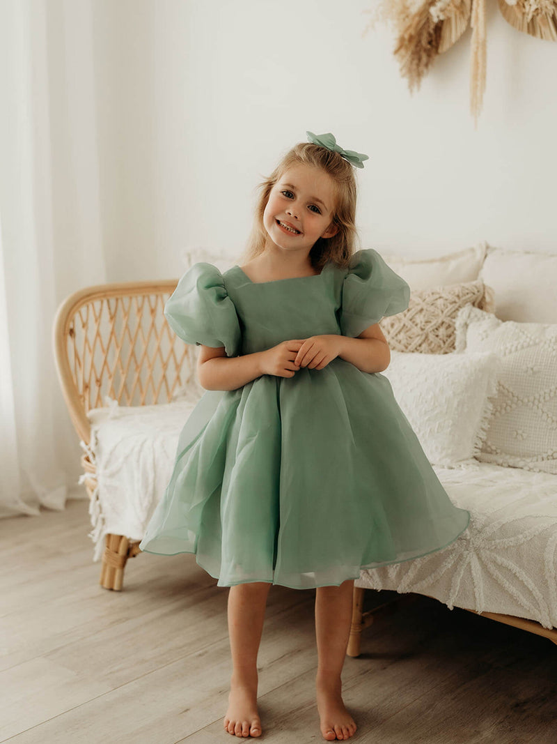 A young girl smiles wearing our Cleo jade green organza puff sleeve flower girl dress.