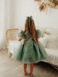 The back of our Cleo flower girl dress in jade, worn by a young girl. Showing the oversized bow at the back and the puff sleeves.