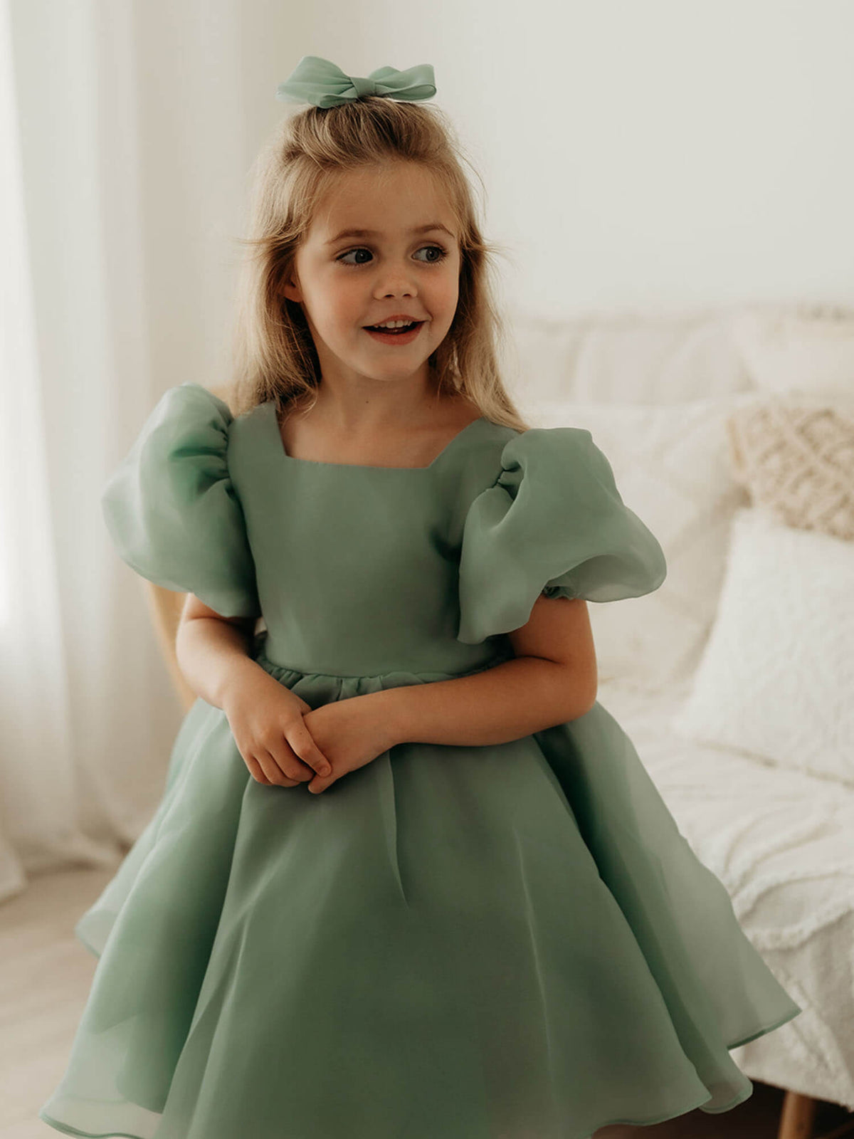 Cleo sage organza puff sleeve flower girl dress and matching organza bow is worn by a young girl.