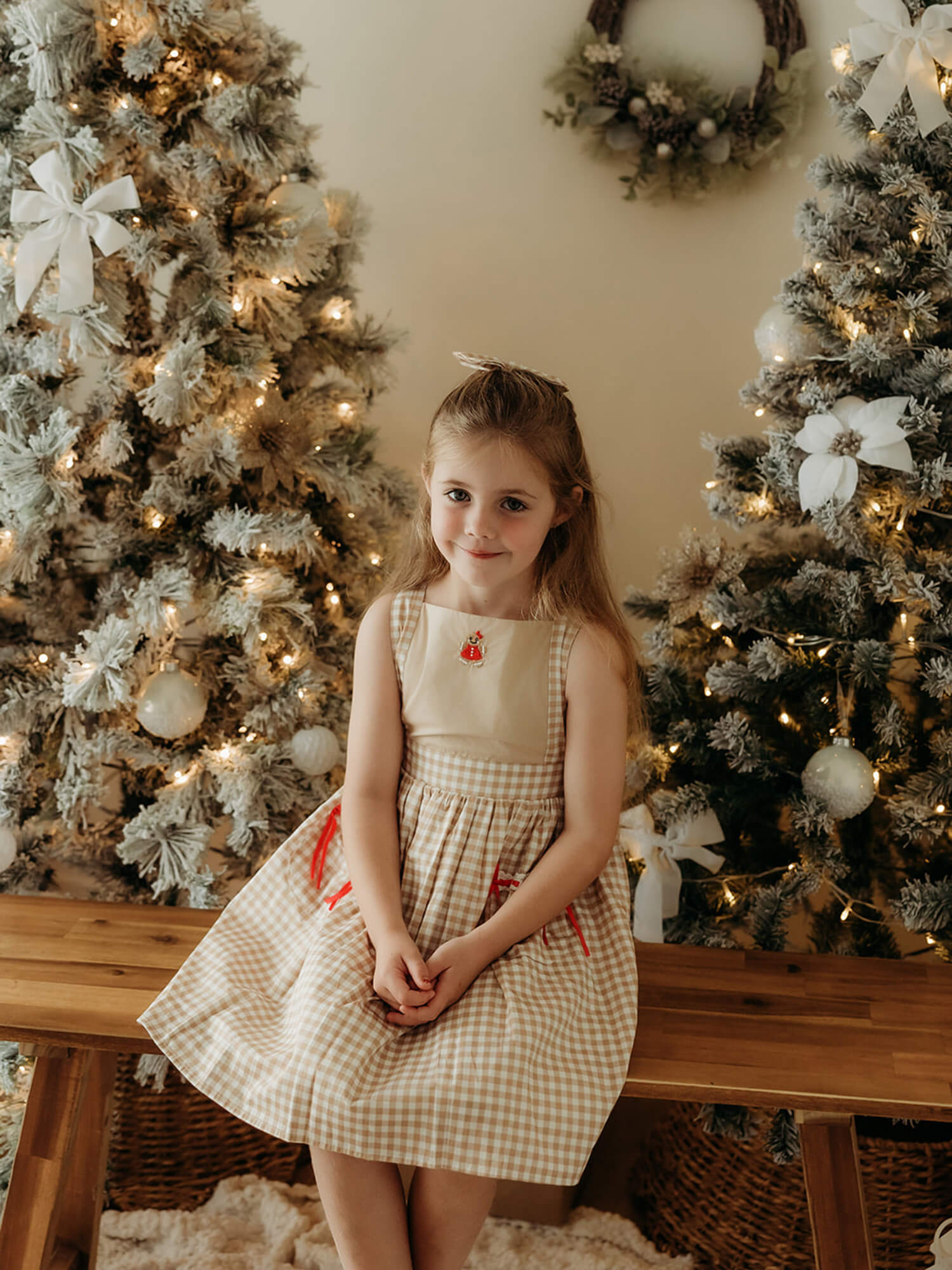A young girl wears our Ellie girls gingerbread Christmas dress with gingerbread plaid and red bows.