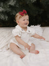 Emma Christmas romper is worn by a baby girl. A perfect Christmas outfit made complete with a crimson bow headband.