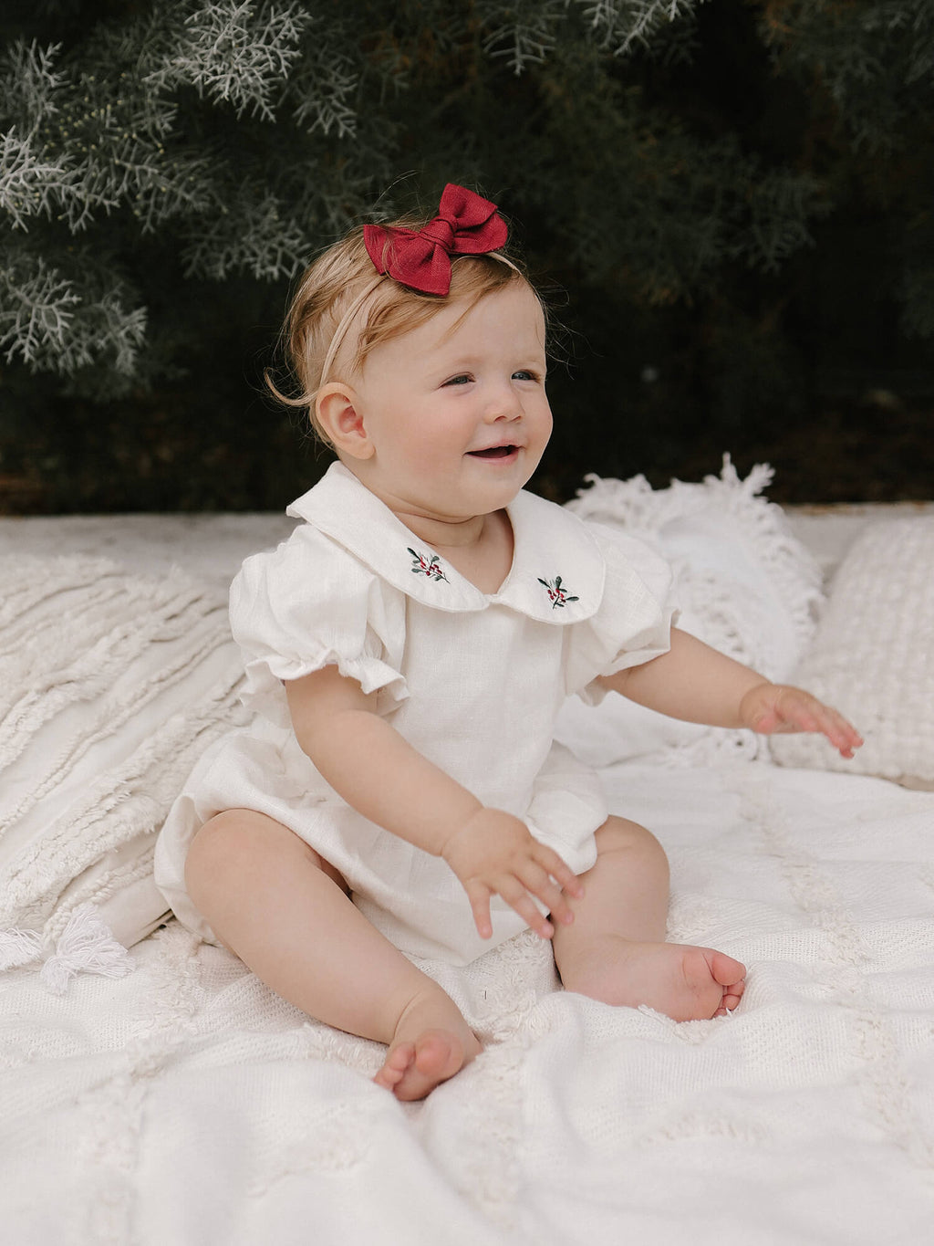 Baby girls Emma Christmas romper is worn by a young baby, she also wears a bow headband.