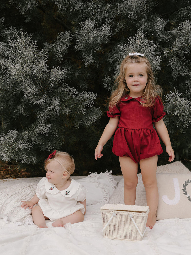 Sisters wear matching Emma Christmas rompers in ivory & crimson.