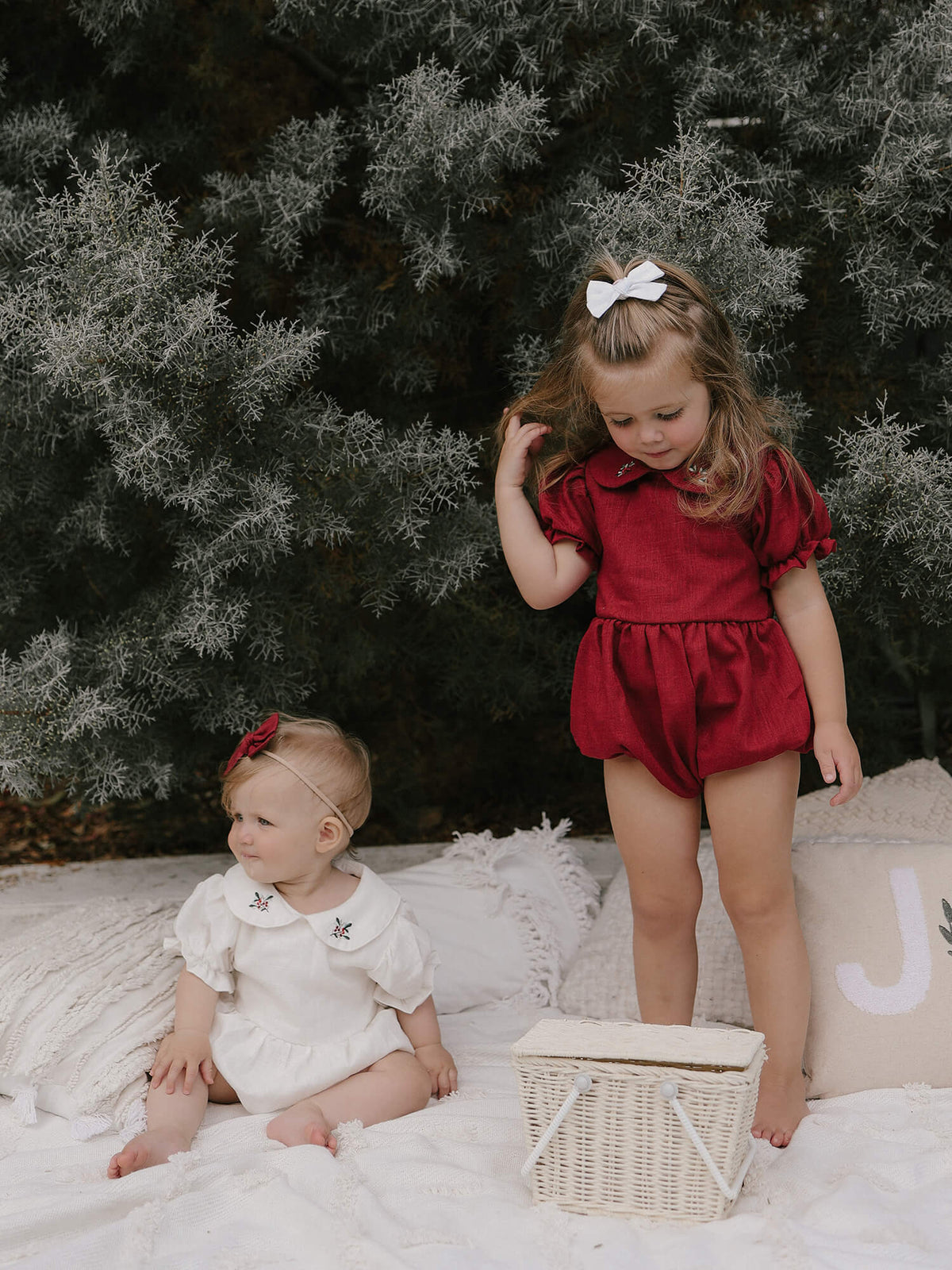 Sisters wears matching Christmas outfits, our Emma linen rompers in ivory and crimson.