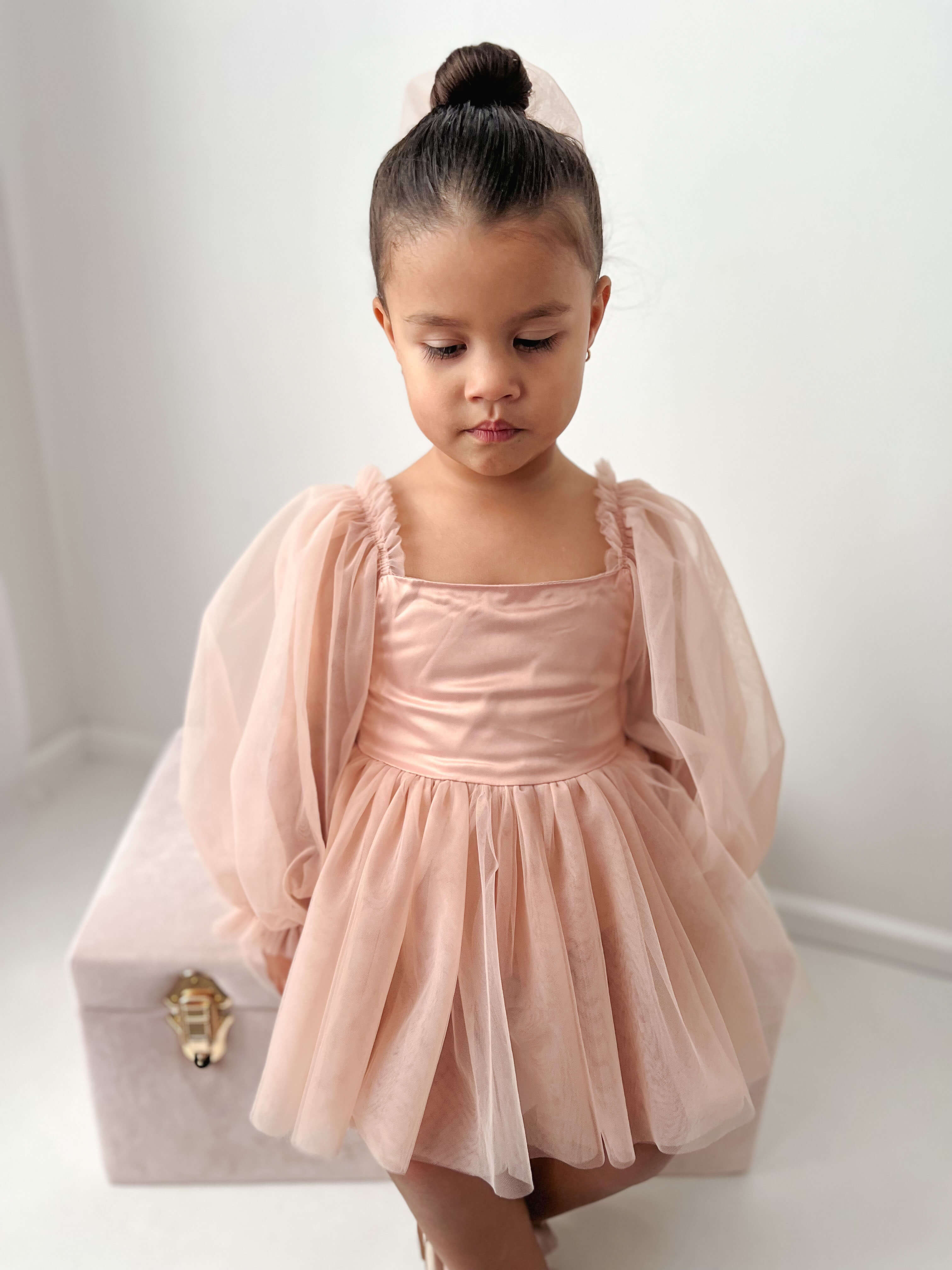 A little girl sits wearing our champagne Eva flower girl romper dress.